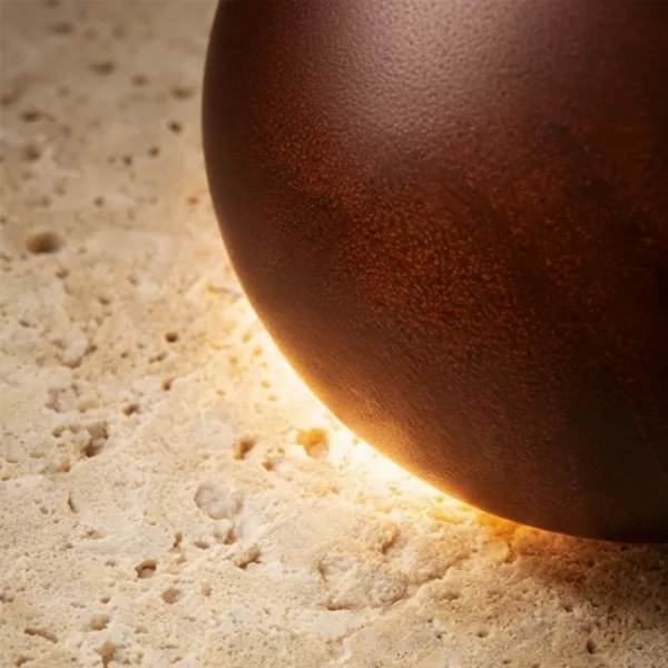 Close-up of the pitted travertine and the dark dome edge lit by the hidden LED of the round wall lamp