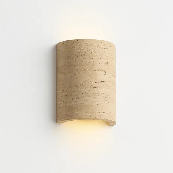 Half cylinder wall sconce in warm beige travertine on a plain white wall, soft light spilling from the open bottom