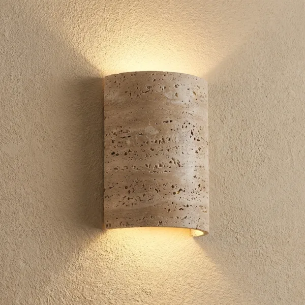 Close view of the travertine half cylinder wall sconce on a textured wall, natural pits visible and light fanning up and down