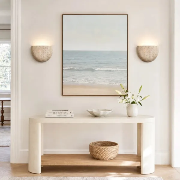 Pair of travertine half-moon wall lights either side of a sea painting above a cream console, a moon wall light pair for a hallway