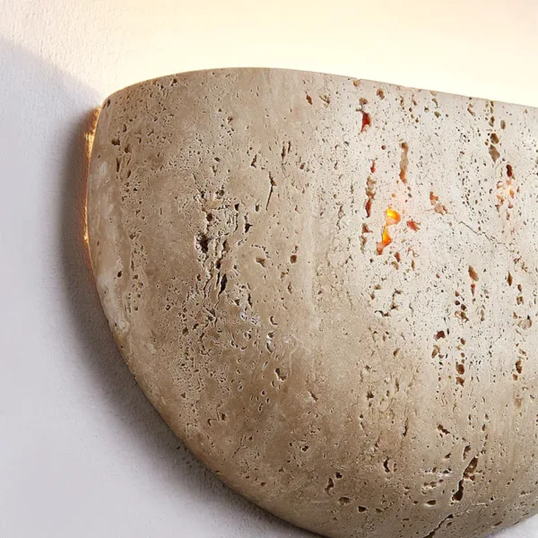 Angled close view of the travertine moon wall light edge, warm light glowing through the stone