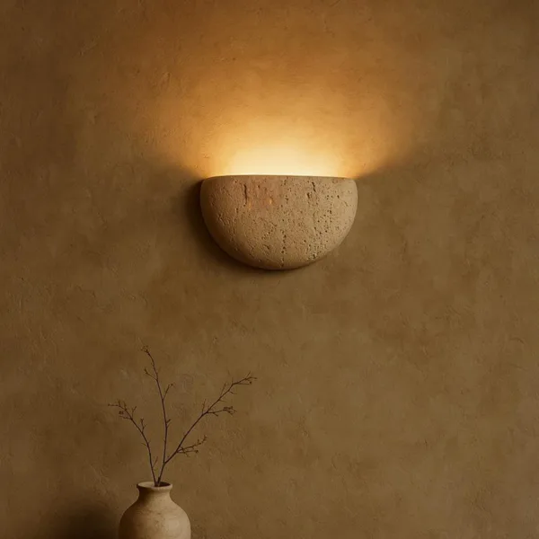 Travertine moon wall light glowing on a dark ochre limewash wall above a clay vase with dry branches