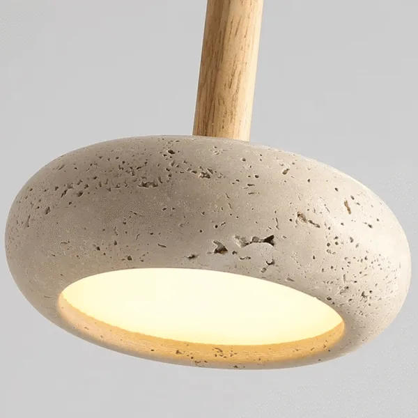 Close-up of the travertine pebble pendant light: pitted natural stone, wood stem and glowing diffuser underneath
