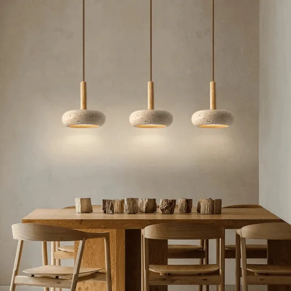 Three travertine pebble pendant lights in a row over a wooden dining table, glowing warm onto the wall