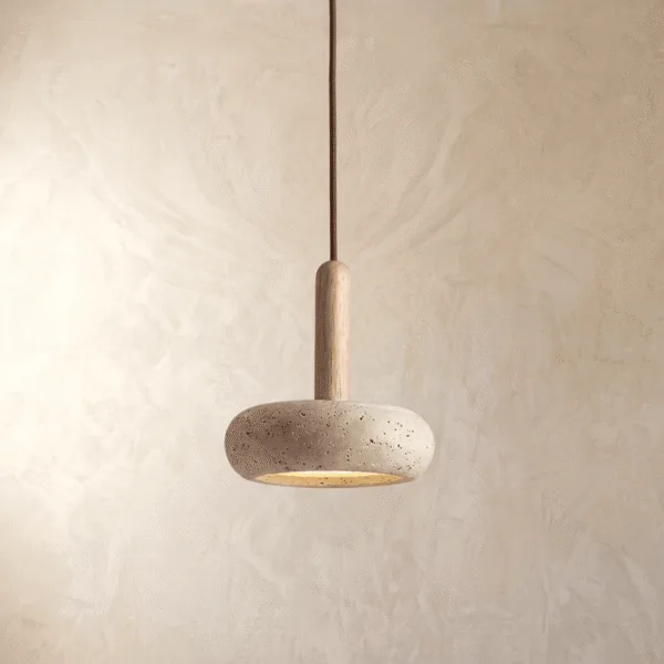 Travertine pebble pendant light with a pitted stone shade and light wood stem, lit warm against a cream plaster wall
