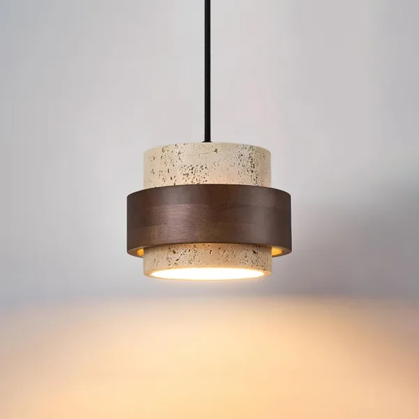 Lit travertine and wood pendant light on a black cord, warm light falling from the stone base onto a grey wall