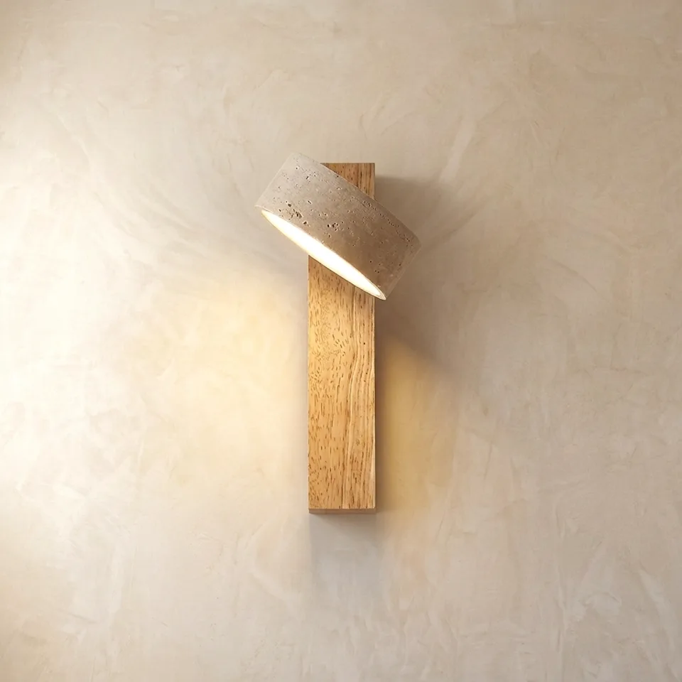 Travertine and light oak wall sconce lit, with the stone head tilted on a plaster wall