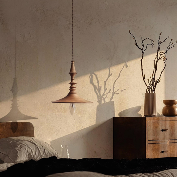 Turned wood pendant light glowing beside a bed and wooden chest of drawers